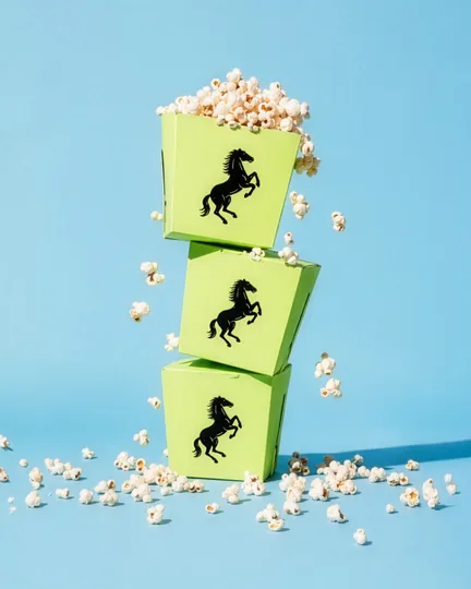 A stack of green popcorn boxes printed with the black horse, popcorn spilling onto a blue set